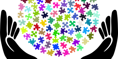 Hände sind wie eine Schale geformt und viele bunte Puzzleteile bilden eine Kugel in der Mitte