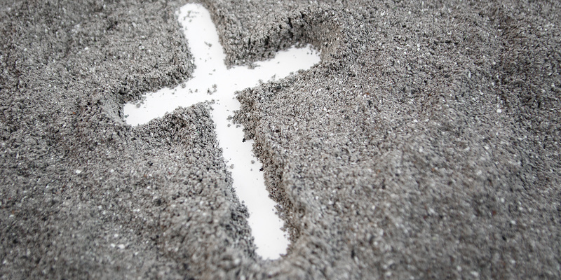 mit Finger gezeichnetes weißes Kreuz auf grauem Asche-Hintergrund