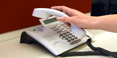 Eine Hand, die den Hörer eines Telefones abhebt.