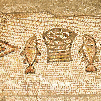 Das berühmte Brot- und Fisch-Mosaik in der Brotvermehrungskirche Tabgha am See Genezareth in Israel: Aus einem Korb ragen vier runde, mit Kreuzen gezeichneten Brote hervor. Links und rechts davon liegt ein Fisch, der gedrungenen Form nach wohl ein Pe
